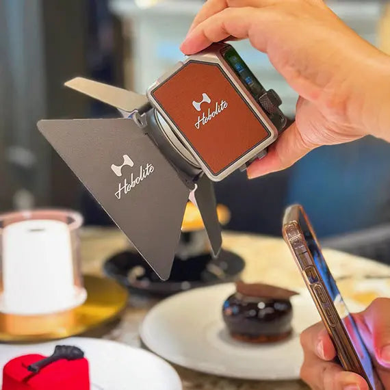 Hobolite Micro LED light with barn doors, held by hand for food photography next to desserts and smartphone.