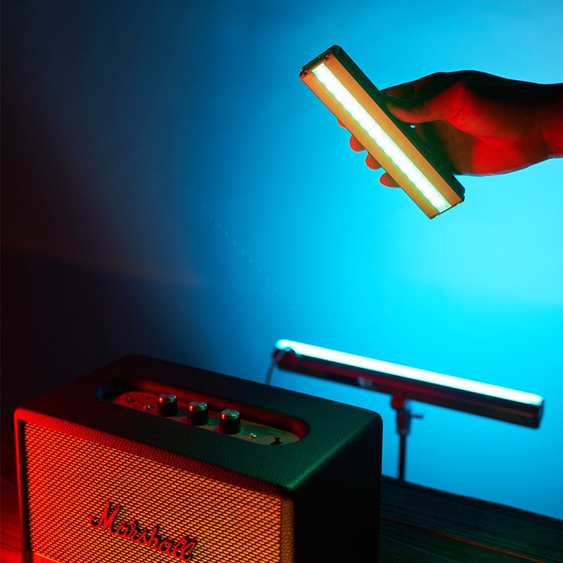 Harlowe Blade RGB tube light held in hand, with another light and Marshall speaker illuminated by blue and red light.