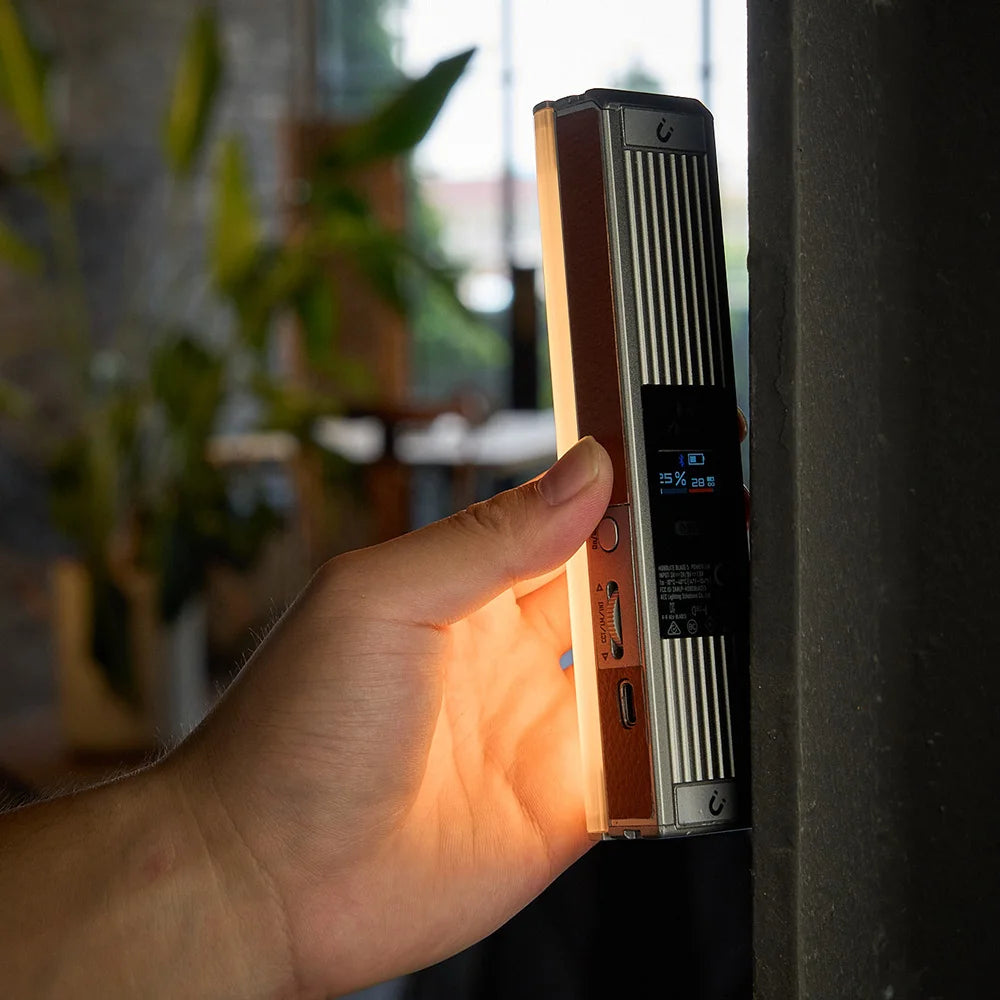 Harlowe Blade 5 tube light held in hand emitting warm orange light, showcasing portability for content creation.