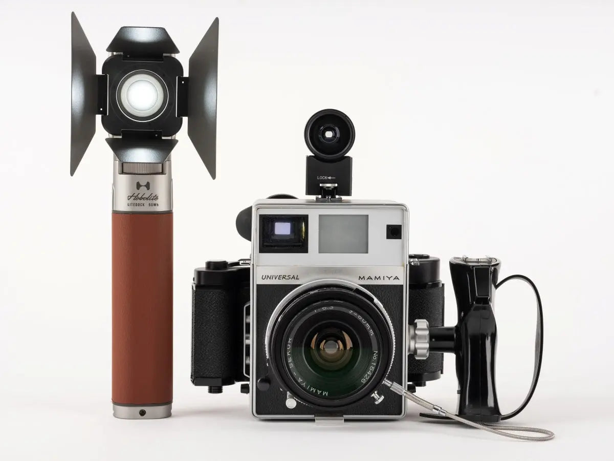 Hobolite LiteDock portable light with brown vegan leather grip next to Mamiya medium format camera on white background.