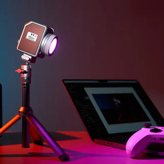 Harlowe Micro RGBCW LED light on tripod with laptop and game controller, creative setup.