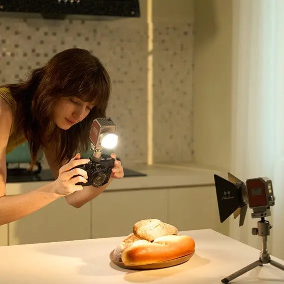Woman uses Harlowe Micro 8W Spectra RGBCW LED light kit on camera for food photography of bread.