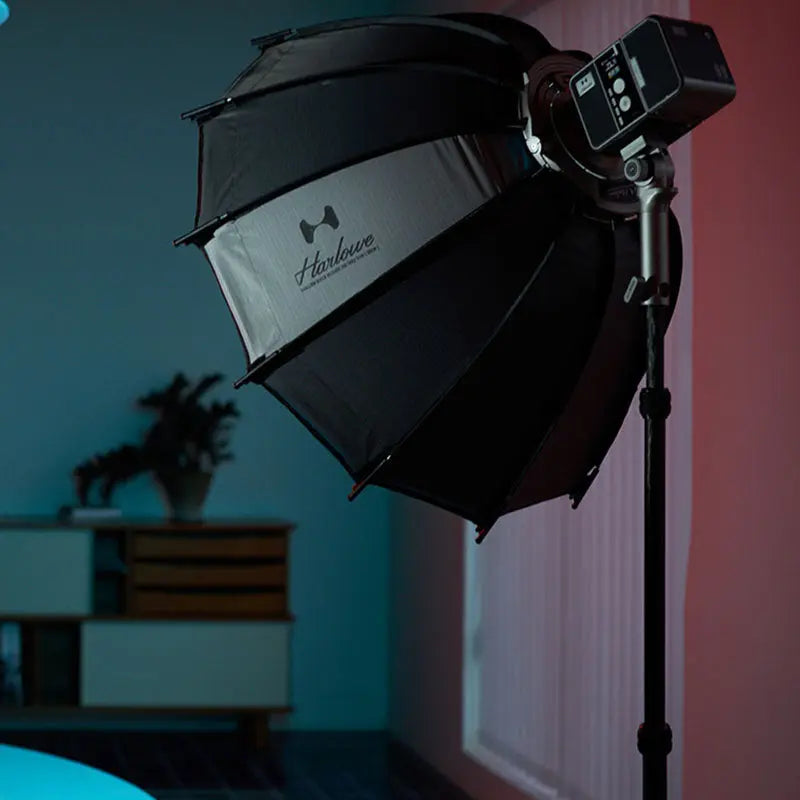 Harlowe Shallow Quick Release Softbox lighting on a stand in a studio setting with blue and pink background lighting.