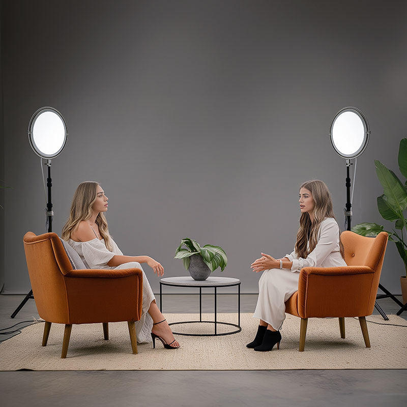 Two women in armchairs being lit by Harlowe Sol 100W round LED panel lights for a video shoot.