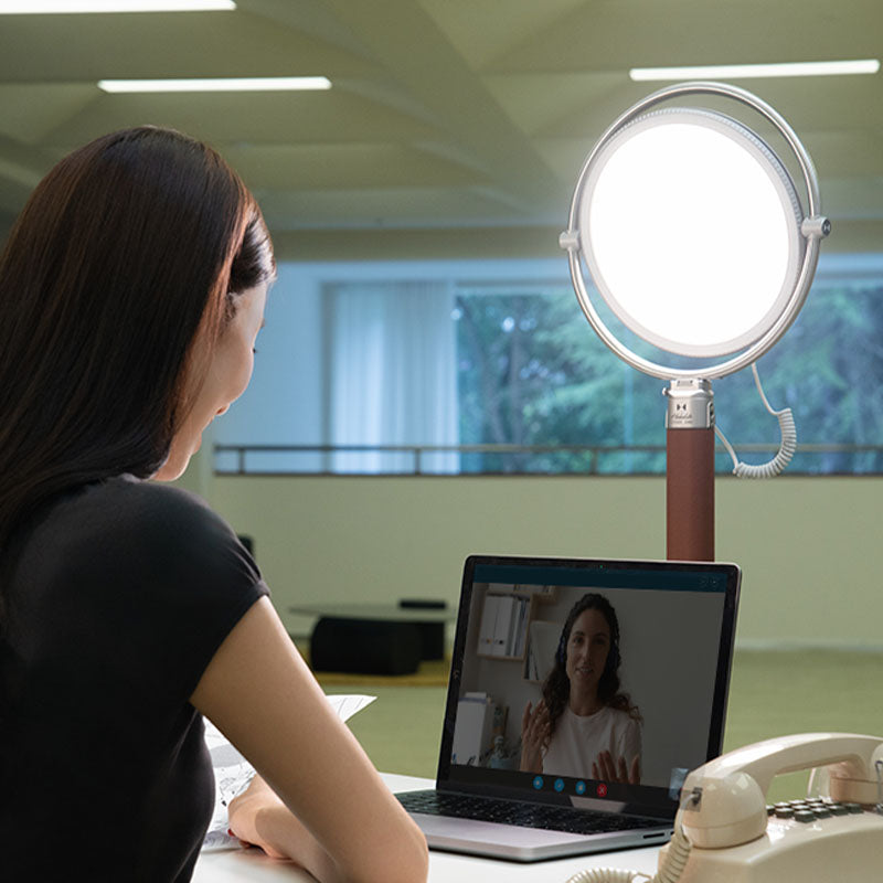 Harlowe Sol LED light illuminates woman on video call, enhancing professional presence.